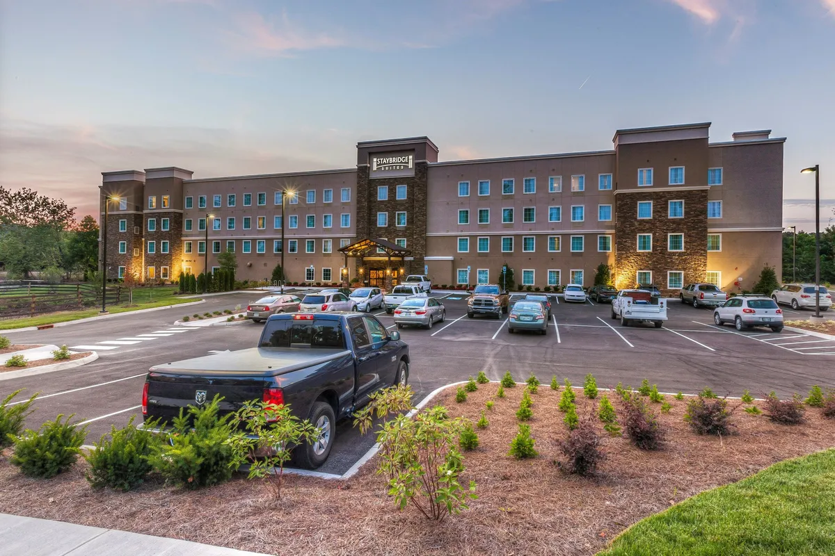 This image displays the hotel entrance of Staybridge Suites Knoxville - West, featuring a landscaped parking area and the inviting facade of the building. The scene is set in soft natural light, creating a welcoming first impression and highlighting the property's accessibility and connection to its surroundings.