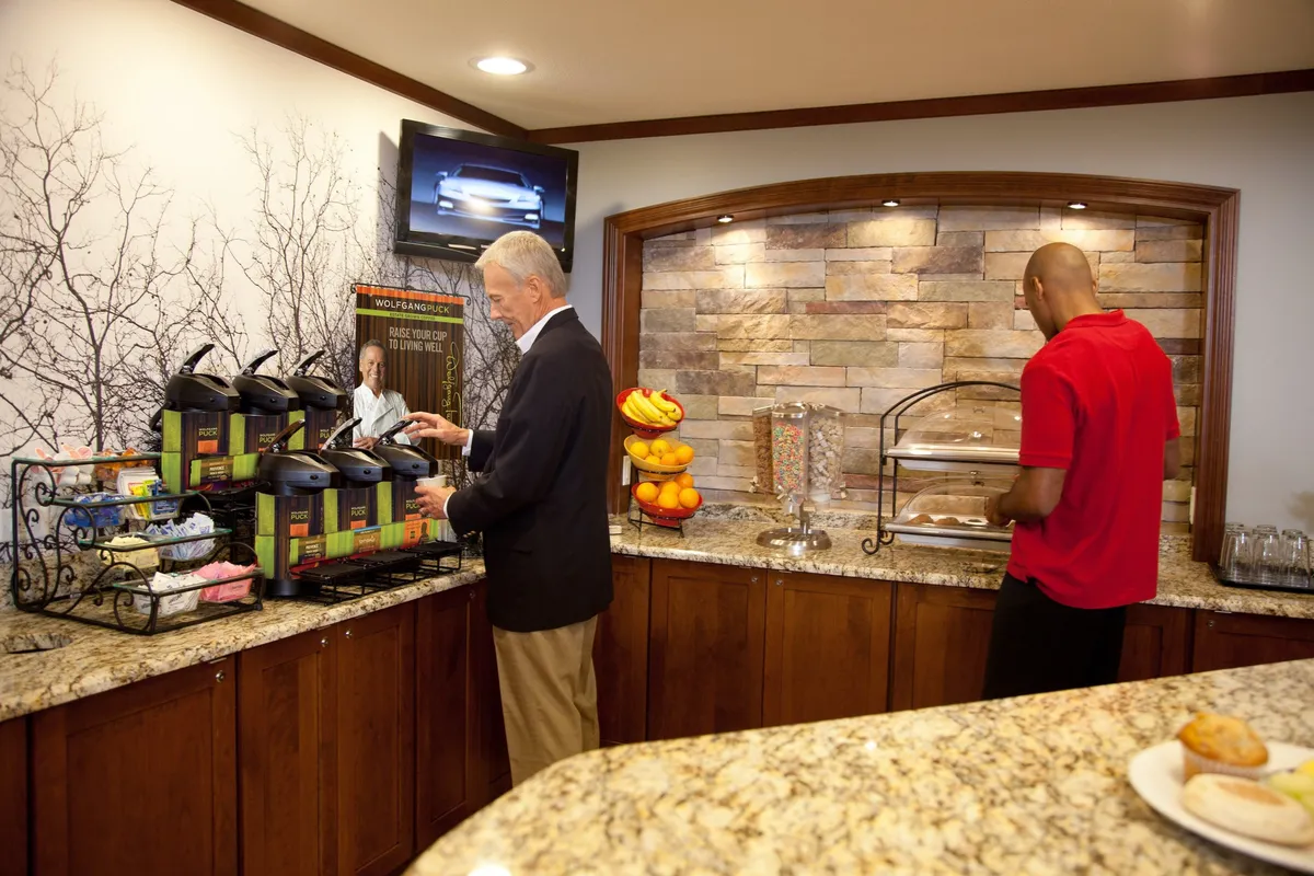 This image displays a welcoming coffee station with a fruit display and pastries on the counter, set against a stone wall. The atmosphere exudes a relaxed morning routine or casual breakfast gathering.