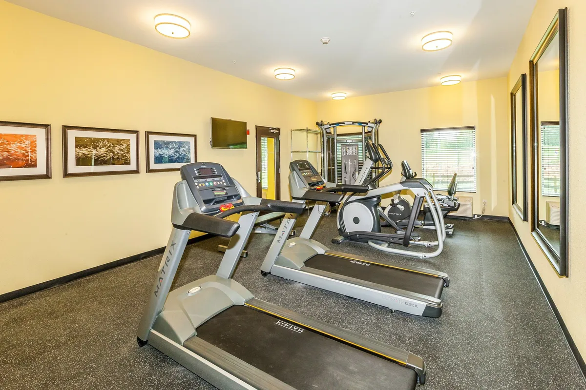 A compact fitness room featuring treadmills, an elliptical machine, mirrors, and modern wall art. The space is energetic yet inviting, offering guests the opportunity to maintain their health and wellness routines during longer stays.
