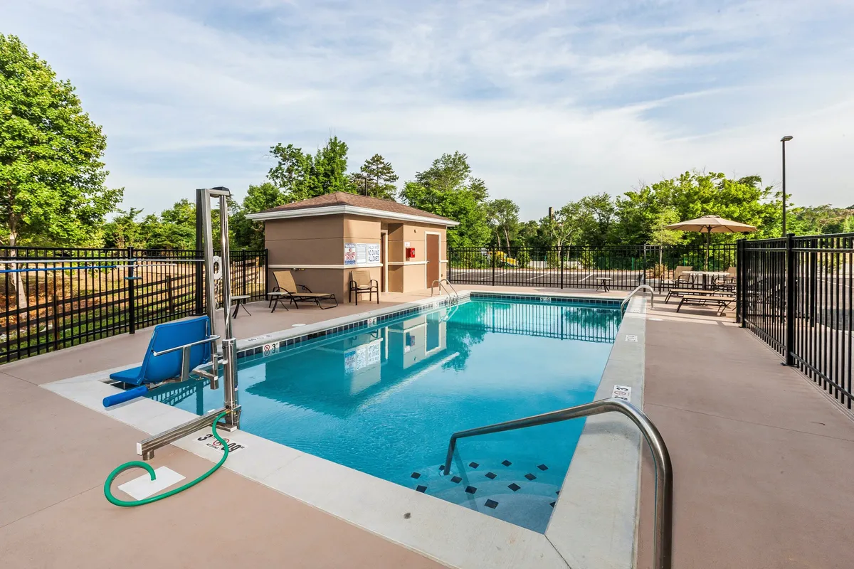 A welcoming outdoor swimming pool area with sparkling water, surrounded by comfortable lounge chairs and shade umbrellas. An access ramp offers easy entry for all family members. The environment feels safe and inviting, perfect for children to enjoy supervised fun while parents relax nearby. The sunset lighting adds a warm, family-friendly atmosphere.