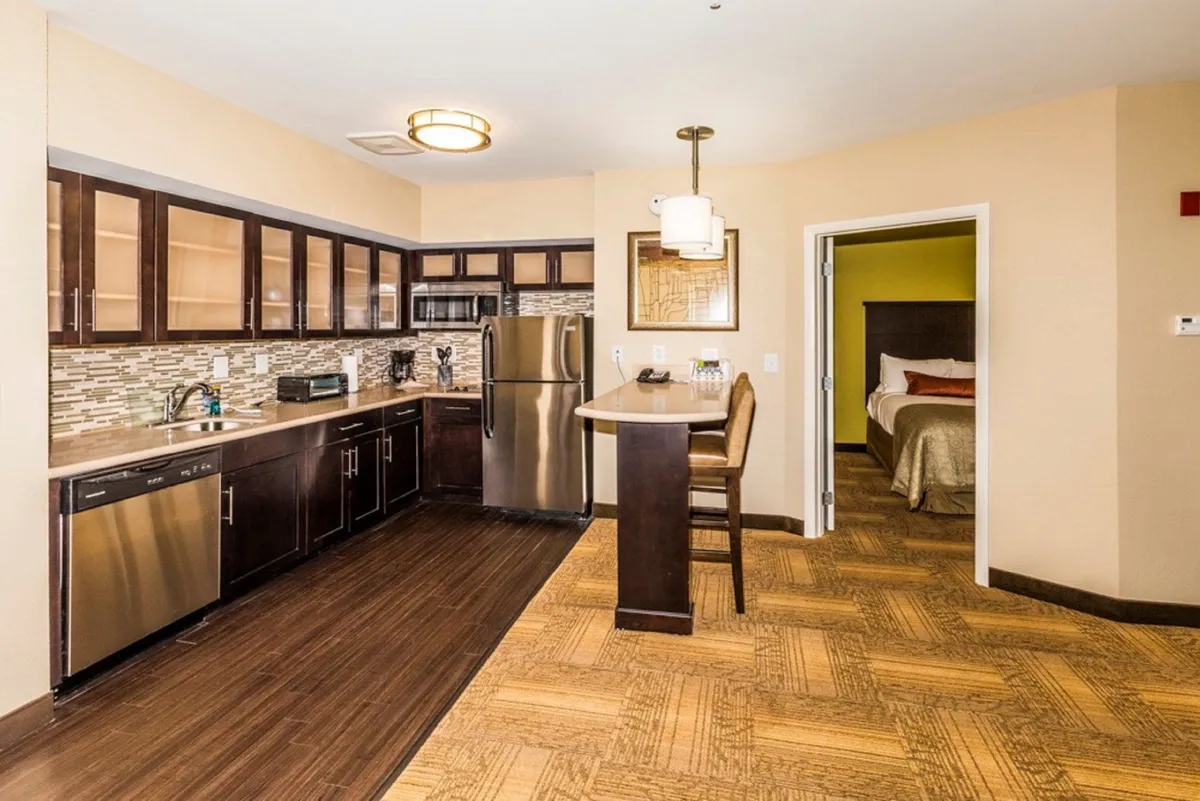 The image spotlights a modern kitchen with stylish cabinetry, stainless steel appliances, and a bar seating area. The layout encourages cooking, entertaining, and casual dining within a compact and manageable footprint. The scene feels inviting, designed for both convenience and social interaction.