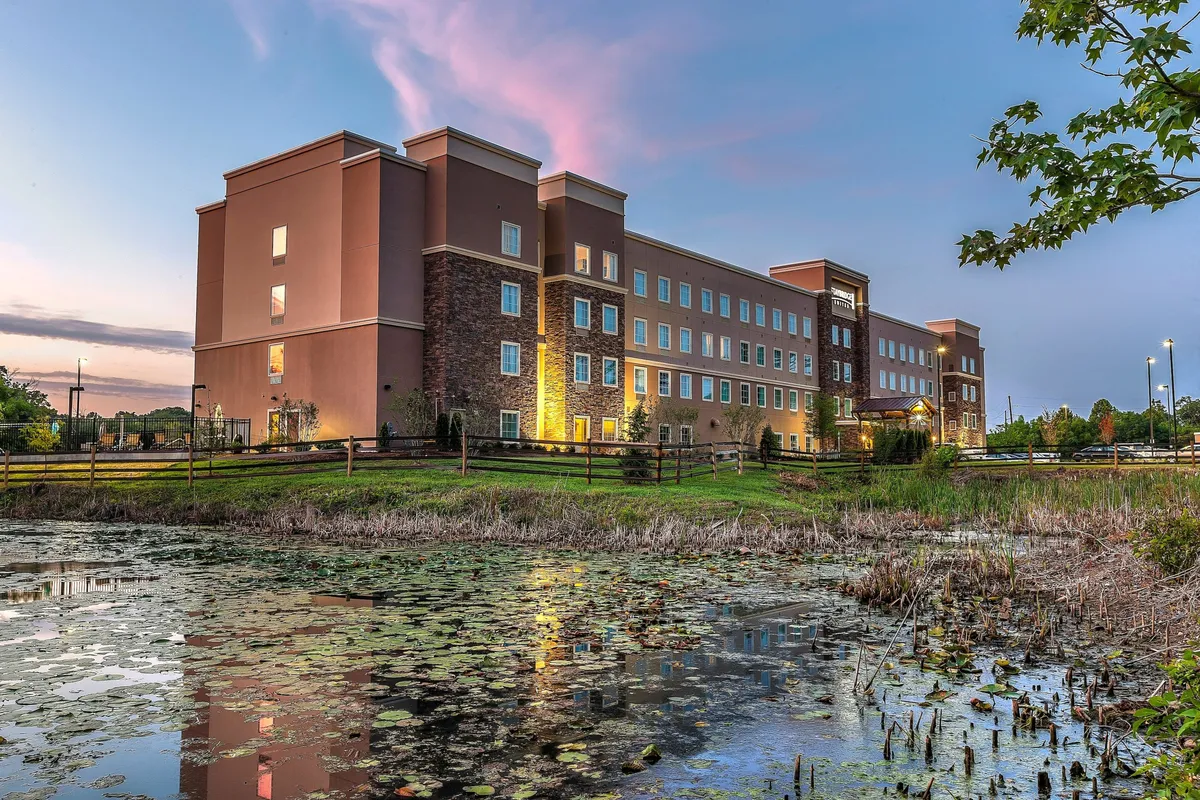 The image captures the hotel’s exterior facade overlooking a serene pond and lush greenery. Guests can be seen strolling along the water’s edge, enjoying the natural beauty and calm ambiance of the Knoxville suburbs.
