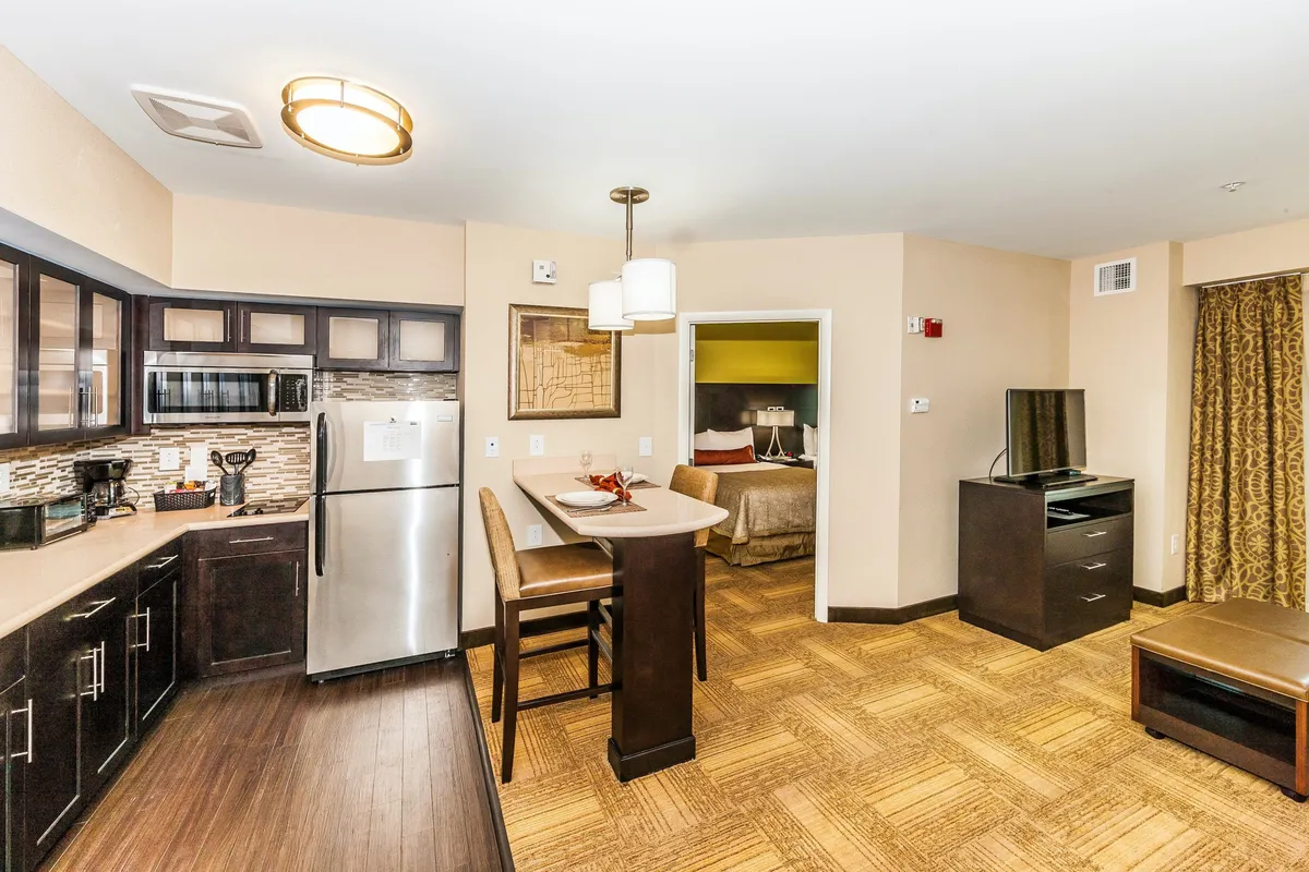 This image presents an open-concept interior where the kitchen, dining table, living space, and a glimpse of the bedroom entrance are all visible. The arrangement emphasizes functional transitions between each area, showcasing a cozy yet practical layout. Natural light and contemporary furnishings contribute to a welcoming, adaptable atmosphere.