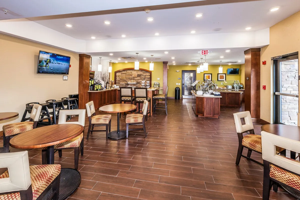 The image features a wooden kitchen counter with a seating area, television, and decorative stone wall. The mood is cozy and welcoming, suggesting a space for both cooking and gathering.