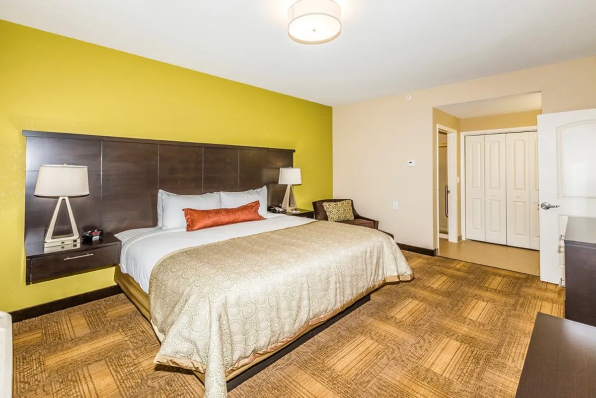 A tranquil bedroom featuring an inviting bed with ornate bedding set against a green accent wall. Nightstands with soft-glowing lamps flank the bed, creating a cozy and restful atmosphere that encourages relaxation and downtime. The thoughtful decor and comfortable touches suggest a space perfect for unwinding after a long day.