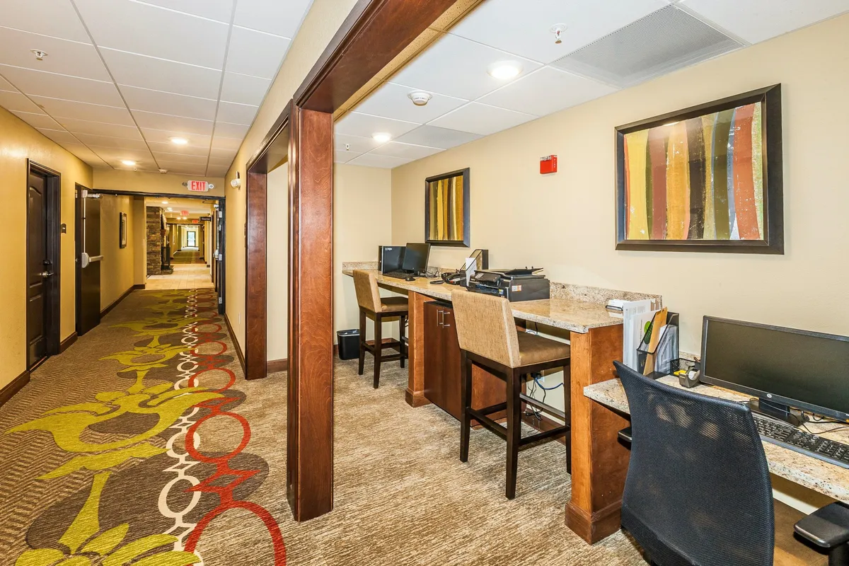 This image showcases a bright interior room equipped with several computer workstations, colorful artwork on the wall, and a decorative carpet. The space is arranged for both productivity and comfort, reflecting a multifunctional area suitable for business travelers or families who want a quiet spot for work, play, or connecting online.