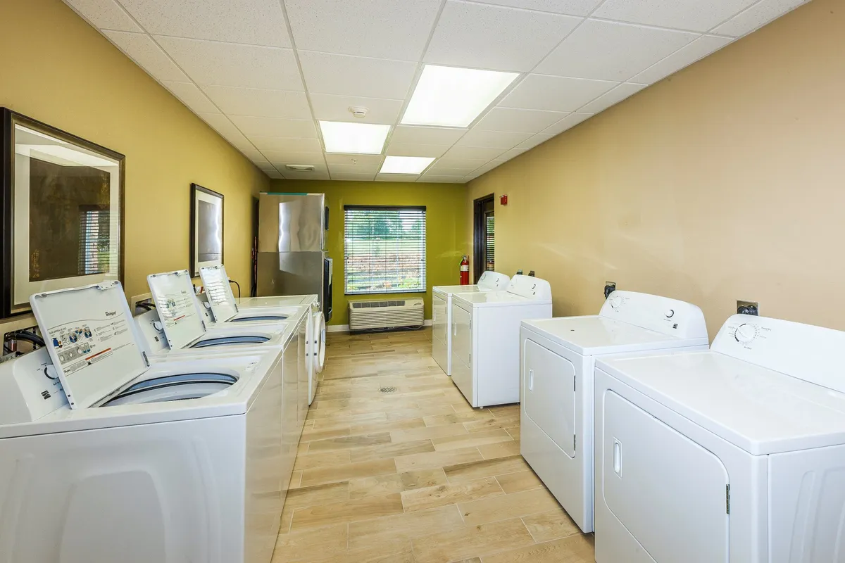 A tidy laundry area with modern washing machines and dryers, illuminated by natural light filtering through blinds. The organized setup suggests ample storage options and thoughtful amenities that support longer stays, ensuring guests’ comfort and convenience.